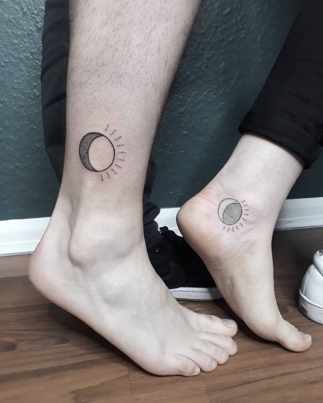 Two ankles with crescent moon tattoos emitting rays radiating out